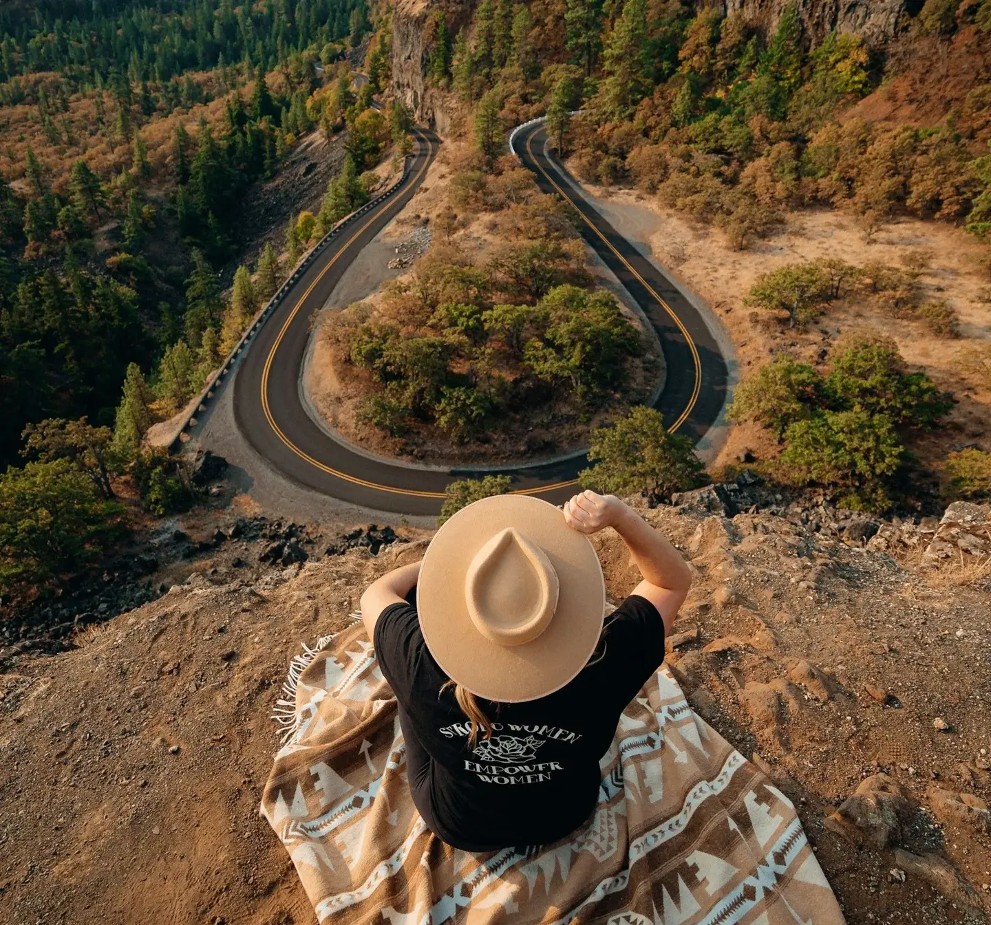 Person sitting on a hill overlooking a curved winding road symbolizing road trip inspiration and travel guides.